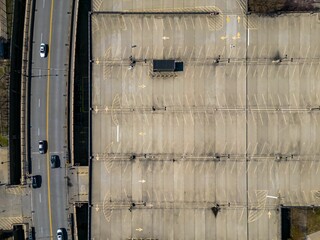 Top down shot over an empty parking lot next to a road with a few cars driving on it