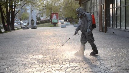 Man in protective suit spraying antiseptic solution on sidewalk in city. Persona disinfecting spray chemicals to preventing spread coronavirus. Sanitary measures in public place. Coronavirus pandemic