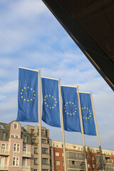 Four European Union Flags Waving with Buildings and Blue Sky as the Background