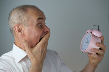 close-up mature man, senior 60 years old holds alarm clock in hand, concept of missing time,...