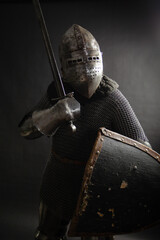 Knight with a helmet in iron armor with a shield and a sword on a black background. Medieval image. studio photo