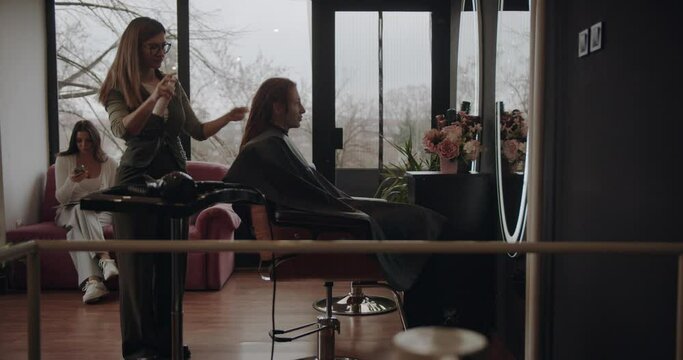 Woman having her hair sprayed with lacquer before new hairstyle at the hair dressing studio