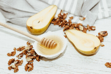 Liquid organic honey in white bowl with pears, wooden honey spoon.