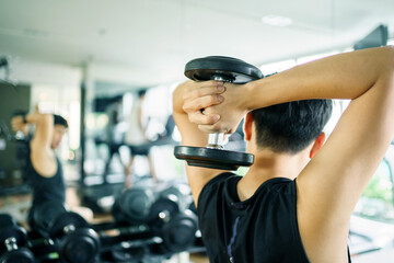 Active Asian sportsman doing a weight training exercise by lifting up a dumbbell, man lifting up or...