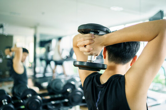 Active Asian sportsman doing a weight training exercise by lifting up a dumbbell, man lifting up or holding a heavy dumbbell in Overhead Tricep Extension position. Bodybuilding workout.