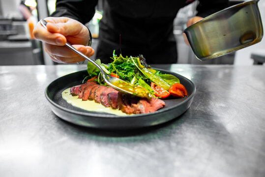 chef hand cooking Roast beef salad with vegetables on restaurant kitchen