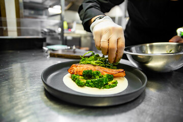 chef hand cooking gourmet salmon steak with broccoli and salad on restaurant kitchen