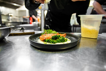 chef hand cooking gourmet salmon steak with broccoli and salad on restaurant kitchen