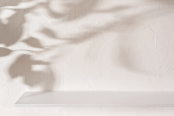 Empty shelf on beige textured plaster wall background with aesthetic floral sun light shadows,...
