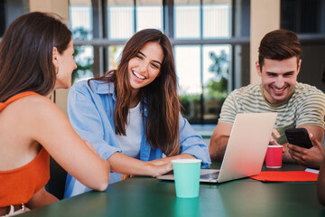 Group of smiling young students using a laptop for research and do the homeworks together at highschool library. three happy caucasian student friends sitting at shool class learning with a computer