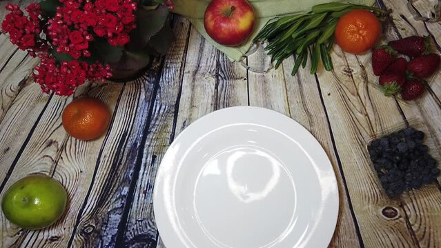 intro. white plate poping on the wooden table with fruits and flowers. Stop motion. High quality 4k footage