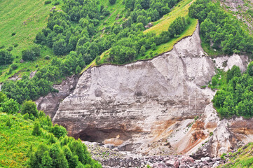 Entrance to a mountain cave in a gorge on a mountainside with trees