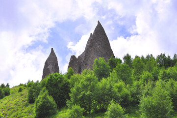 Sharp rocks against the sky with clouds on a mountainside with trees