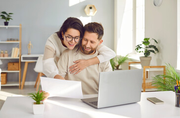 Happy young couple is planning an apartment renovation and home design project with laptop looking at architecture plan. People working together in home office. Couple teamwork startup concept.