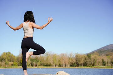 Young woman in balance practices yoga outside with lotus pose backward. Mountains landscape. Yoga day.