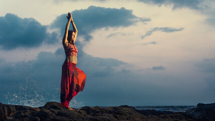 Young beautiful healthy woman making meditation on the rocks, sunset on the sea. Arambol, Goa, India. - obrazy, fototapety, plakaty