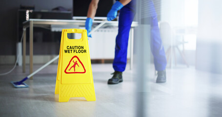 Male Janitor Cleaning Floor With Caution Wet Floor Sign