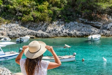 Naklejka premium Young woman in beach clothes and sun hat looking at beautiful beach with boats and turquoise sea