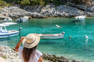 Young woman in beach clothes and sun hat looking at beautiful beach with boats and turquoise sea