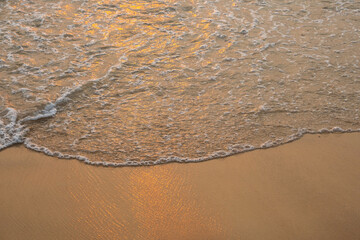 Sea wave foam on sandy beach in sundown light, close up. Tropical summery background.