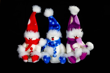Three handmade toy snowmen with hats and scarves on a black background. Made of felt, scarf, black button, close up. Decor. Christmas and New Year concept