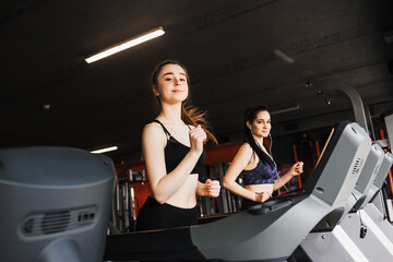 Young pretty sporty girl trains her muscles in the gym by running on a treadmill.