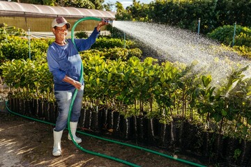 Vertical shot of a black woman wearing a cap tending to a garden while watering the plants