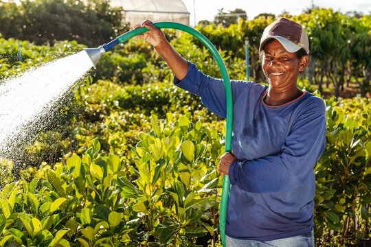 Vertical shot of a black woman wearing a cap tending to a garden while watering the plants