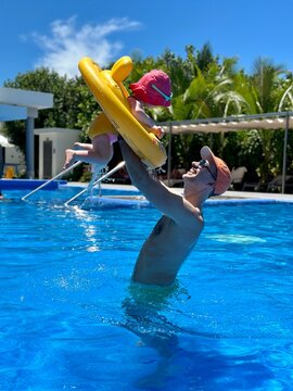 Bébé ou enfant fille d'un an et demi souriant dans sa bouée jaune dans une piscine jouant avec son papa