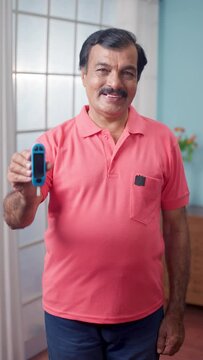 Vertical shot of Happy Indian elderly senior man showing suger level checking glucometer by looking at camera - concept of Healthcare, happines and diabetes.