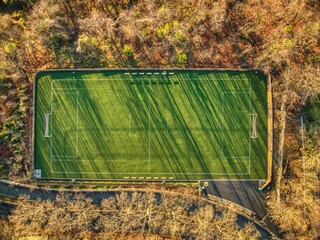 Aerial top view of an empty soccer field surrounded by lush green trees in a forest setting - Powered by Adobe