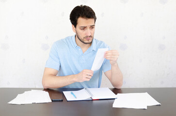 Close up of unhappy man sitting at the table, stressed and confused by calculate expense from...
