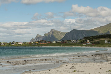 Fototapeta na wymiar View on Rambergstranda during summer with mountains and houses in the background. Sandy beach in the foreground. Waves, beach, Norway, Nordic, Lofoten
