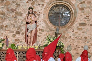 Group of people wearing red hooded cloaks standing in front of a statue of Jesus.