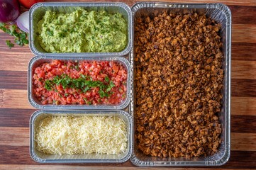 Variety of ingredients in multiple containers used to create a Mexican dish, such as tacos