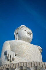 Low-angle shot of a marble statue of Buddha against a backdrop of a deep blue sky.
