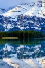 Trees and snowy mountains reflected in calm Two Jack Lake in Alberta, Canada
