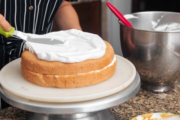 Female baker adding cream to a freshly-baked cake