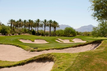 Scenic landscape featuring a lush green golf course with sand bunkers scattered across the fairway