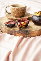 Tropical summer breakfast still life. Mangosteen fruits and tea cup on wooden tray.