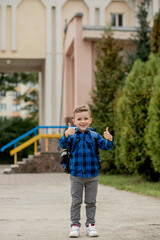 Fototapeta na wymiar Cheerful mischievous Caucasian schoolboy in blue shirt and school jacket posing showing approval gesture, class. Back to school.