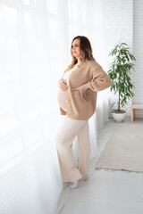 a beautiful pregnant woman with long hair stands near the window in a large bright living room