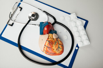 Stethoscope, clipboard, pills and heart model on a table