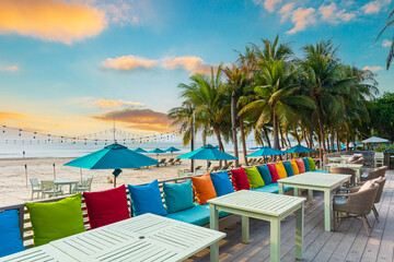 Seaside restaurant,Beach club concept, food corner or cafe, restaurant tables, straw natural chairs, wooden tables, makrome knitted sun umbrellas, white modern sun beds, sea view on background
