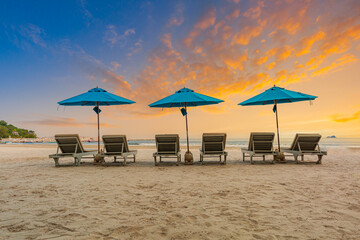 Beaches and sun tables in Thailand,Row of empty sun loungers and orange parasols on the tropical beach at sunset. Vacation in the all inclusive hotel on the Caribbean sea 