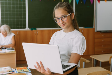 cute smiling teenage girl posing with laptop at classroom