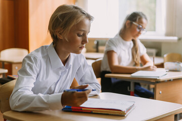 Fototapeta premium teen students writing in copybook at desk in classroom, looking at camera