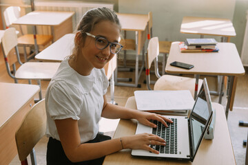 cute smiling teenage girl posing with laptop at classroom