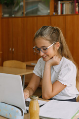 smiling teenage girl in glasses working at laptop in classroom