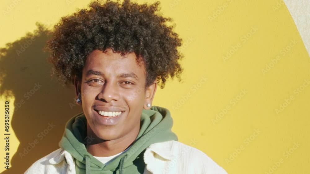 Sticker Young happy African American teen guy laughing on yellow wall lit with sunlight. Smiling cool ethnic generation z teenager student model standing looking at camera posing for portrait outdoors.